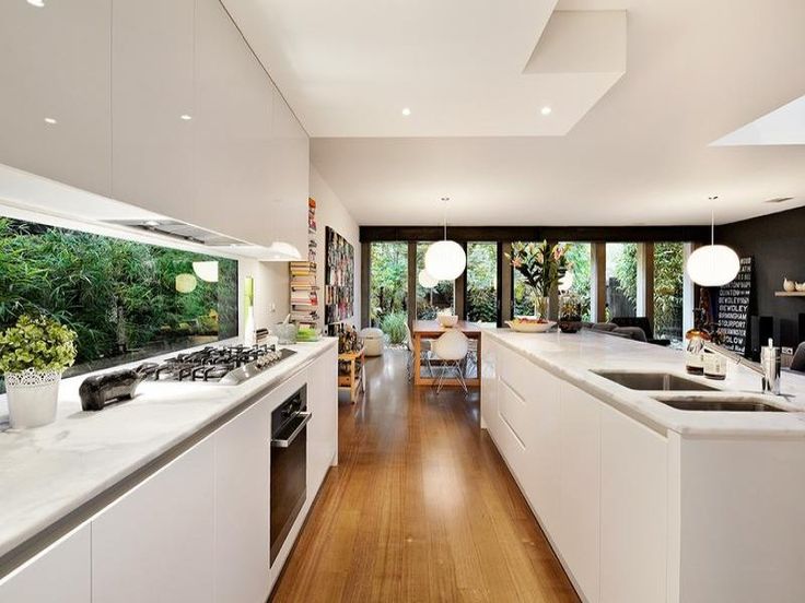 a minimalist white kitchen with sleek cabinets, built in lights and a window backsplash that lets enjoy greenery in the garden is amazing