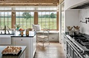 a cozy farmhouse kitchen with white cabinets, black countertops, vintage fixtures, a large black cooker and a glazed wall that shows off a field