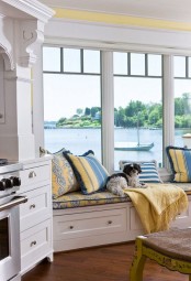 a white vintage farmhouse kitchen with chic cabinets, stainless steel appliances and a bay window with a gorgeous sew view, plus a windowsill daybed to enjoy it
