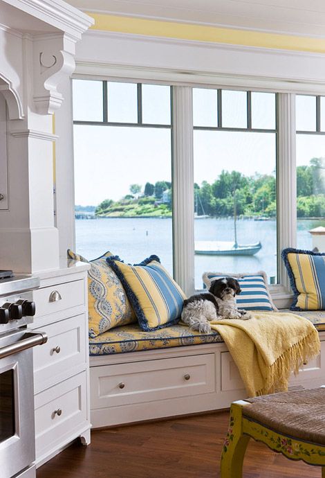 a white vintage farmhouse kitchen with chic cabinets, stainless steel appliances and a bay window with a gorgeous sew view, plus a windowsill daybed to enjoy it
