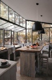 a jaw-dropping wabi-sabi kitchen with glazed walls and partly ceiling to merge with the forest outside, reclaimed and aged wood and concrete furniture and black pendant lamps