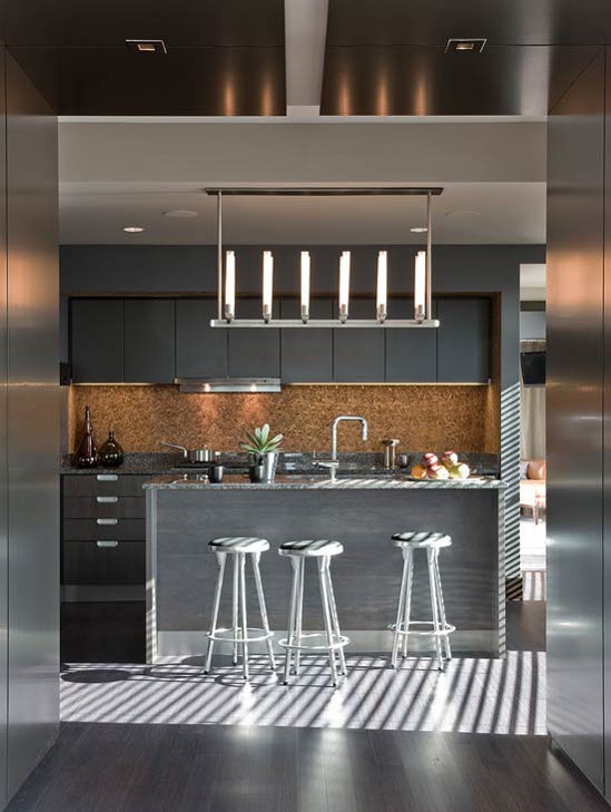 a contemporary grey kitchen with sleek cabinets, a pendant lamp, stools and a large kitchen island plus a cork backsplash