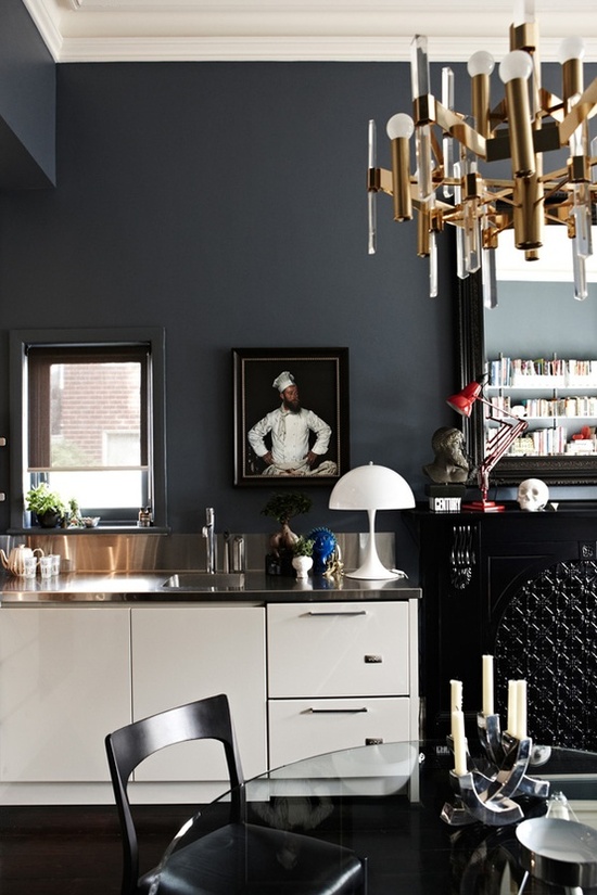a dark eclectic kitchen with white cabinets, refined chandeliers and artworks, matte grey walls
