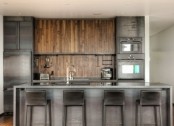 an industrial kitchen with metal cabinets and appliances, a wooden backsplash and cabinets, a metal kitchen island and stools for a masculine feel