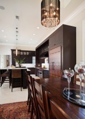 a rich-stained wooden kitchen with white countertops, white backsplashes and lamps and woven stools