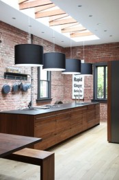 an industrial kitchen with red brick walls, black pendant lamps, a large kitchen island a black countertop
