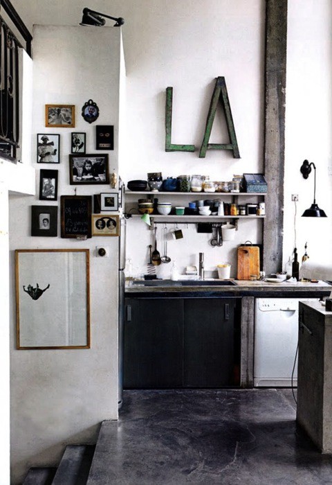 a constrating kitchen with black cabinets, white shelves, rough wooden furniture, a gallery wall and tableware
