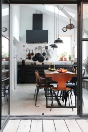 a black metal kitchen with pendant lamps, a black hood, rich-stained wooden dining set is very eye-catchy