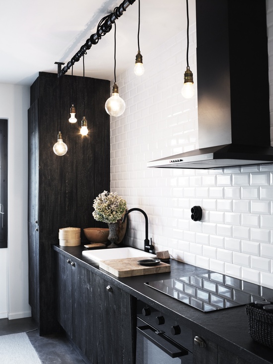 a Nordic black and white kitchen with dark furniture, white subway tiles and hanging bulbs looks bold and chic
