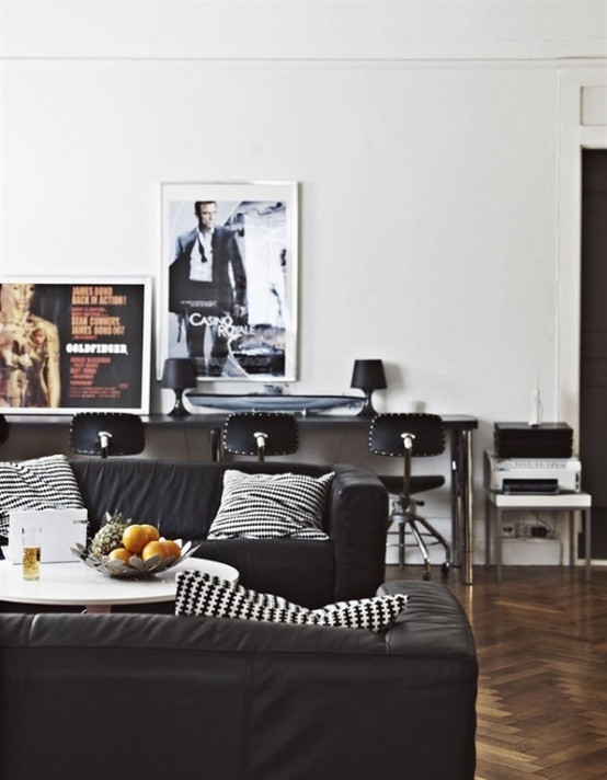 a stylish living room with black upholstered furniture, chairs and pillows, artworks and a desk with chairs by the wall