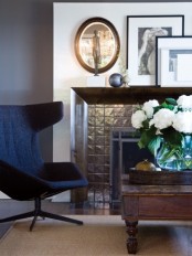 a stylish corner with a black chair, a tile clad fireplace, a wooden coffee table and artworks on the mantel