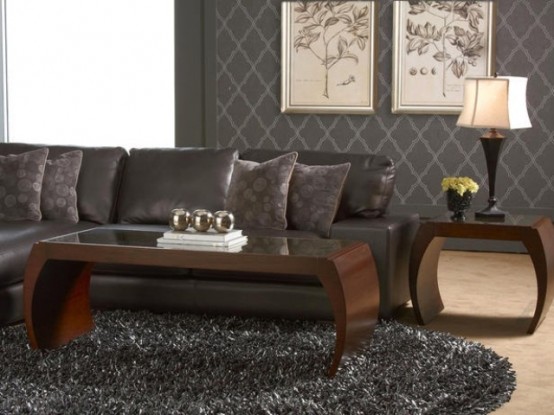 a dark living room with grey furniture, wooden tables, artworks, a fur rug and lamps