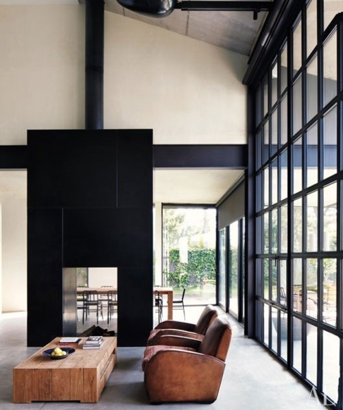 a contemporary living room with a glass wall, a black tile stove, leather chairs and a wooden coffee table