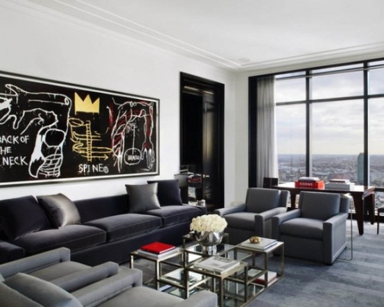a contemporary masculine living room with dark upholstered furniture, some glass tables, an artwork and a glass wall for views