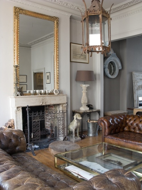 a sophisticated living room with leather furniture, a stone fireplace, refined lamps and glass tables plus a giant mirror