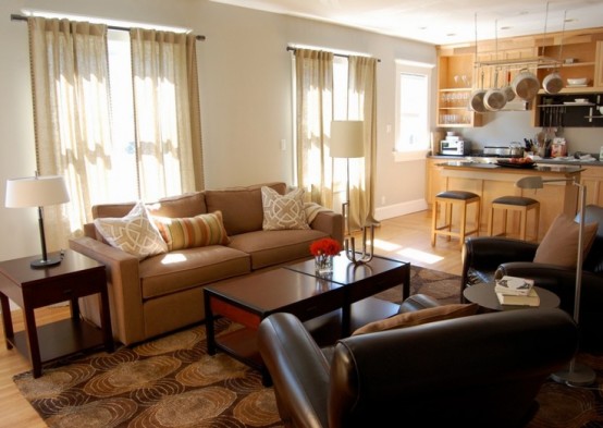 a cozy living room with leather furniture, lamps, a wooden table and a rug plus a matching kitchen area
