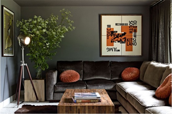 a stylish dark living room with dark walls, an L-shaped sofa, orange pillows and a graphic artwork, a floor lamp and a wooden coffee table