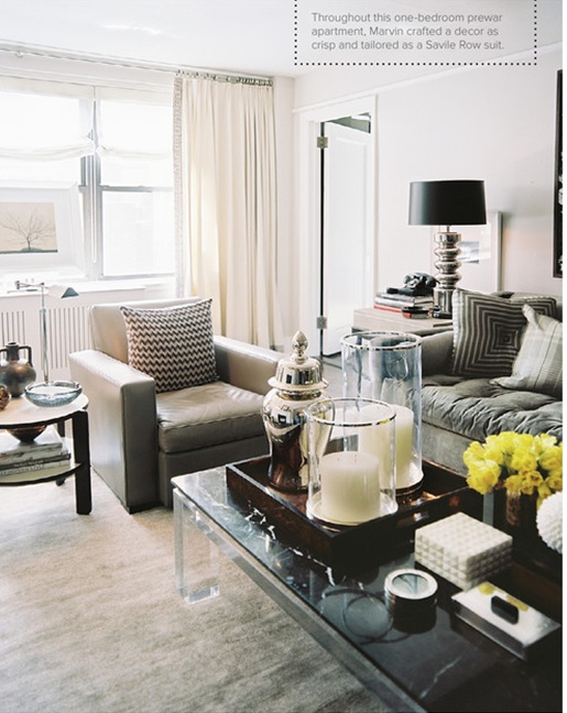 a neutral masculine living room with leather upholstered furniture, an acrylic table, neutral textiles and a black lamp