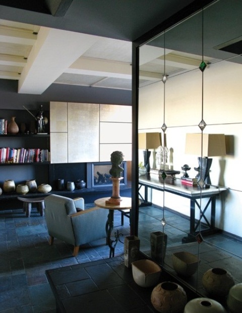 a dark living room with dark walls, an upholstered chair, a sleek storage unit on the wall and a large mirror