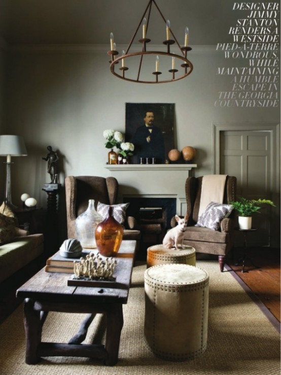 a moody living room with grey walls, a fireplace, cozy upholstered furniture, a rough wooden table and a chandelier