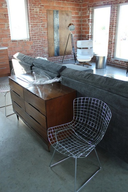 an industrial living room with brick walls, upholstered furniture, a wooden sideboard, metal lamps and a coffee table plus a wire chair