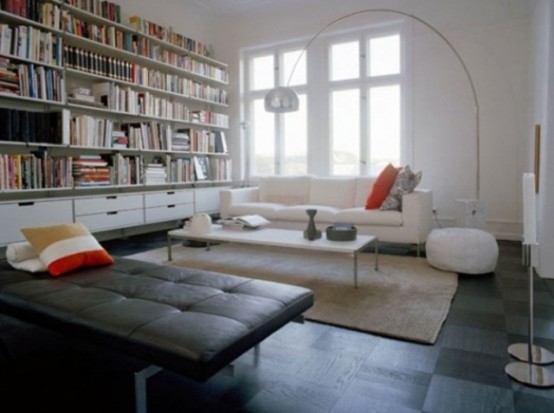 a contemporary living room with neutral and black upholstered furniture, floor lamps and a large bookshelf