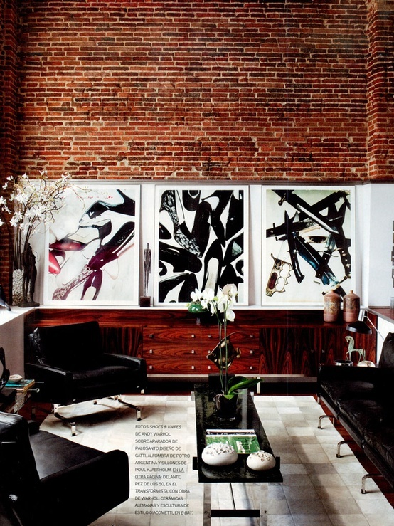 a sophisticated masculine living room with brick walls, artworks, black leather furniture and some blooms
