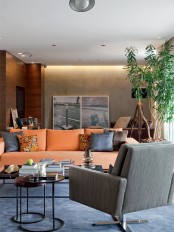 a bright modern living room with orange furniture, printed pillows, a potted plant, artworks, a floor lamp and coffee tables