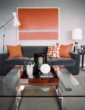 a bright modern living room with a grey sofa, a colorful artwork and matching pillows plus a glass coffee table and neutral lamps