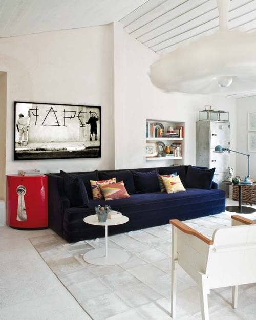 a neutral living room with a navy sofa and a red side table for a touch of color, artworks and storage units plus lamps