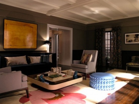 a dark living room with grey walls, neutral and dark upholstered furniture, an artwork, a rug and a blue ottoman