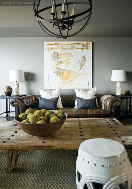 a stylish masculine space with grey walls, a leather sofa, a wooden coffee table, a metal sphere chandelier and artworks