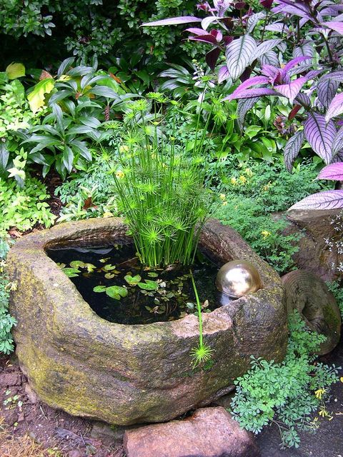 a rough stone bowl with greenery and a gold ball is a nice and catchy idea of a mini pond for outdoors