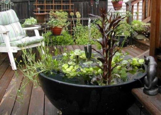 a mini pond in a black plastic tub, with greenery, cane and other plants for decorating an outdoor space