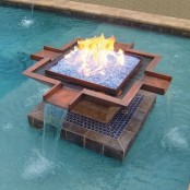 a super creative and spectacular fire bowl placed right in the pool, with a waterfall built in is a gorgeous idea for a garden, two elements in one