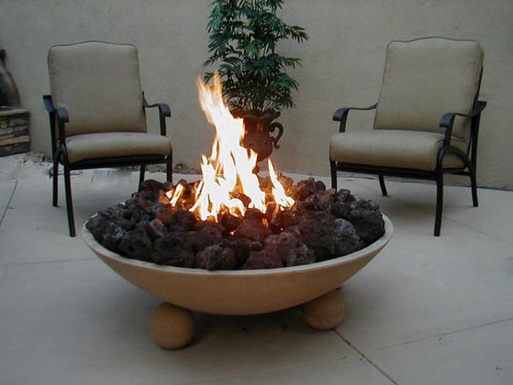 an elegant outdoor sitting space with lovely leather chairs, a stone firebowl with rocks inside and a plant is a lovely space to spend an evening