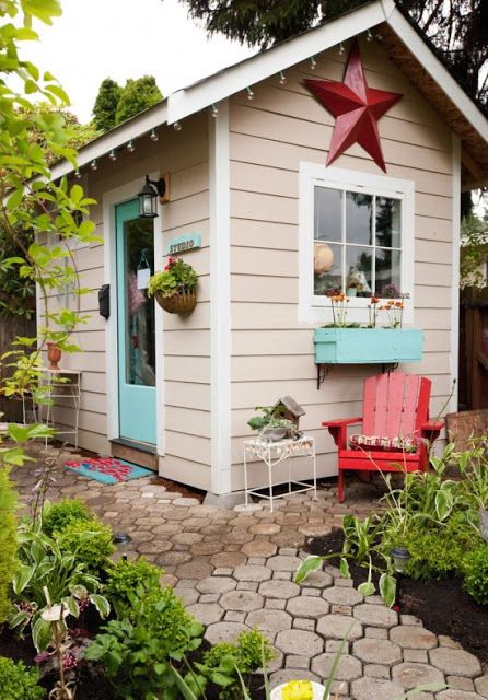 a tan kids' house clad with siding, with a turquoise door and a window with a turquoise planter and blooms looks like a real personal house