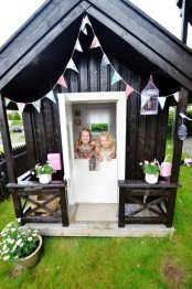 a Nordic black and white kids’ playhouse with a pastel garland, a cage, potted blooms and a pink watering can is amazing for any kids’ games
