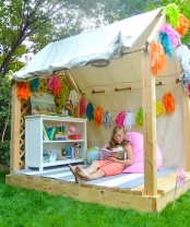 an outdoor kids’ playhouse with cool furniture, a colorful rug and a beanbag chair, some tassels and bright decor is amazing