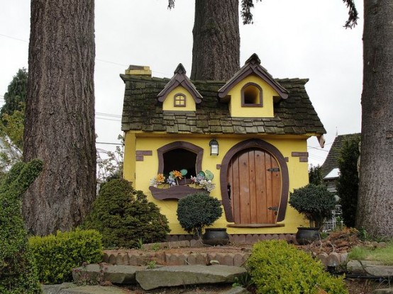 a tiny fairytale-like kids' playhouse in yellow, with a dark roof, dark window frames and a cute door reminds of hobbits' houses