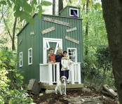 a small green planked kids’ playhouse with white window frames and a door, with some signs is great for building it in the woodlands