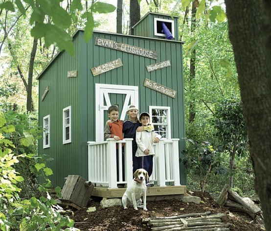 a small green planked kids' playhouse with white window frames and a door, with some signs is great for building it in the woodlands