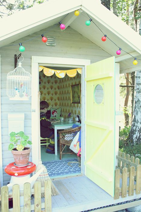 a pastel kids' playhouse with vintage furniture, colorful garlands, a cage, potted blooms and greenery and colorful garlands