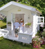 a white kids’ playhouse with carved touches, a white interior and potted blooms looks like a real one