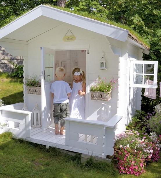 a white kids' playhouse with carved touches, a white interior and potted blooms looks like a real one
