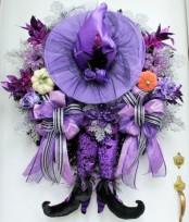 a creative lilac and purple Halloween decoration with a lilac witch hat, witch’s legs, pumpkins, blooms, ribbons and faux foliage is wow