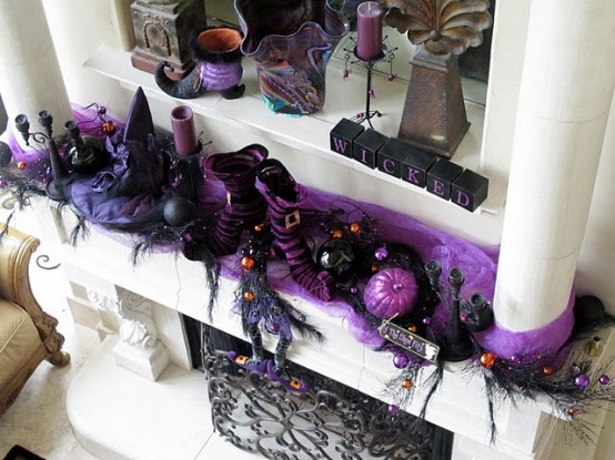 a bold purple and black Halloween mantel with pumpkins, witches' legs and hats, candles, berries on branches and much other stuff