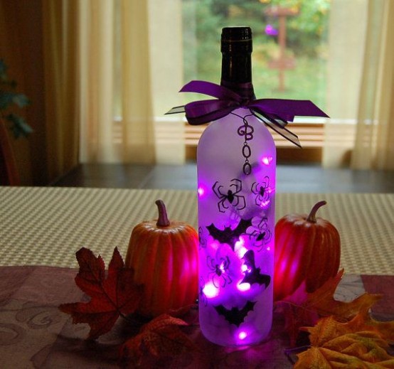 a Halloween centerpiece of a bottle with bats and purple lights, pumpkins and leaves is a cool idea for Halloween