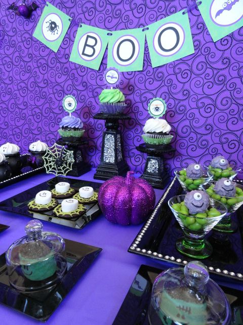 a bright purple, green and black Halloween sweets table with a glitter pumpkin, spiderwebs and various monsters is a very creative and fun idea for a kids' Halloween party
