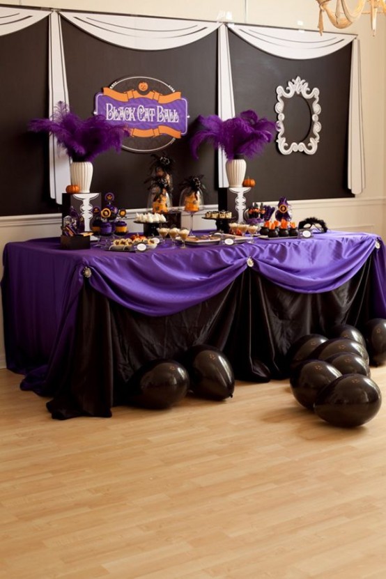a black and purple Halloween table with purple feathers, tablecloths, blakc balloons and various colorful sweets